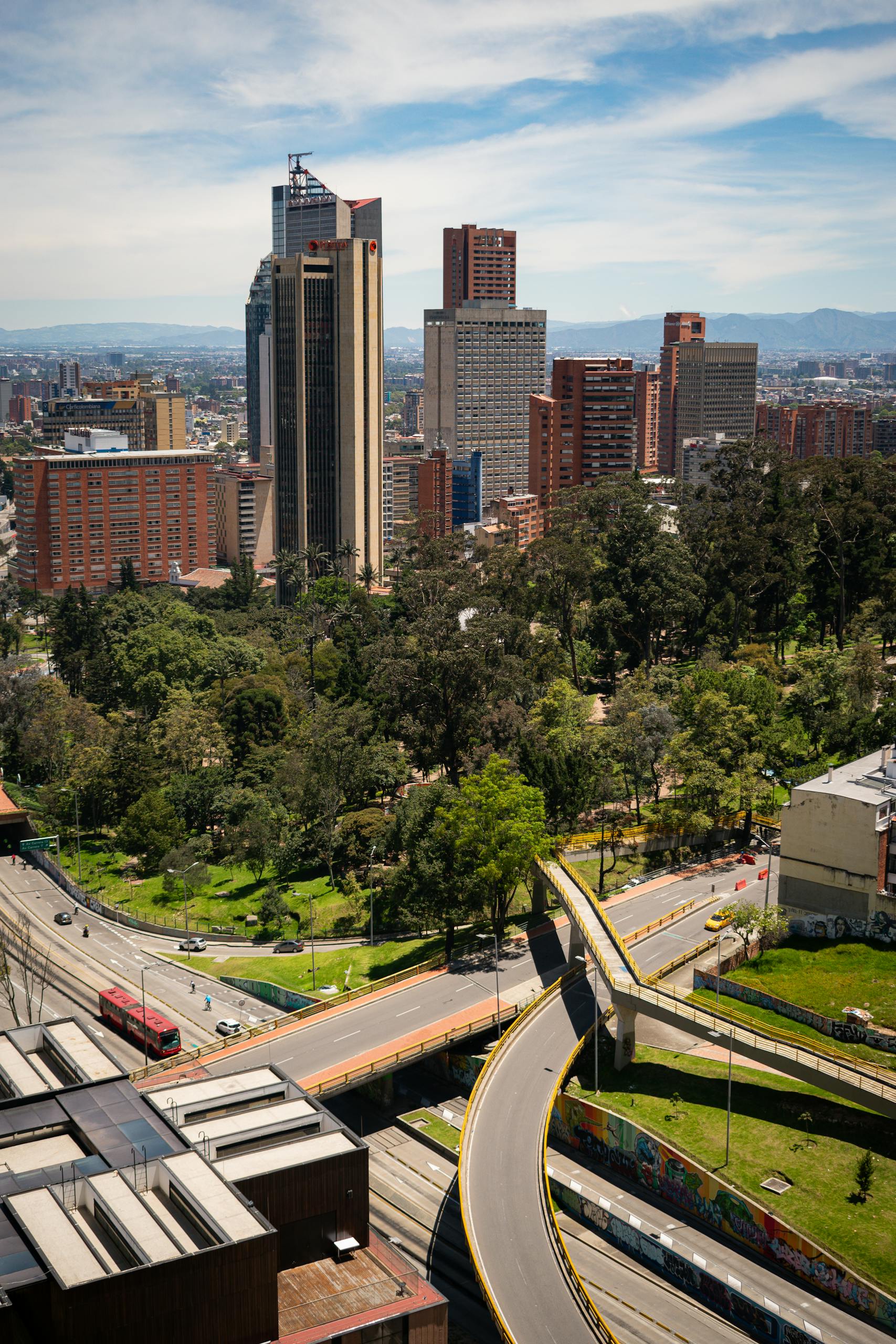 Aerial view of Bogotá featuring skyscrapers, roads, and green spaces under a clear sky.